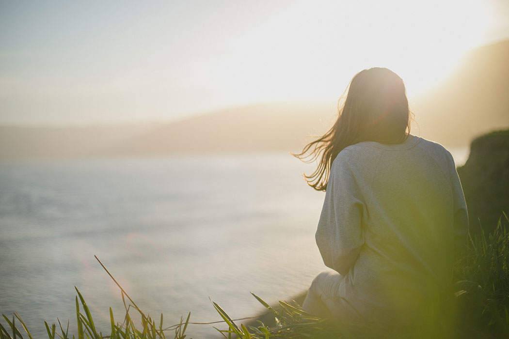 Woman sitting on cliff overlooking the ocean